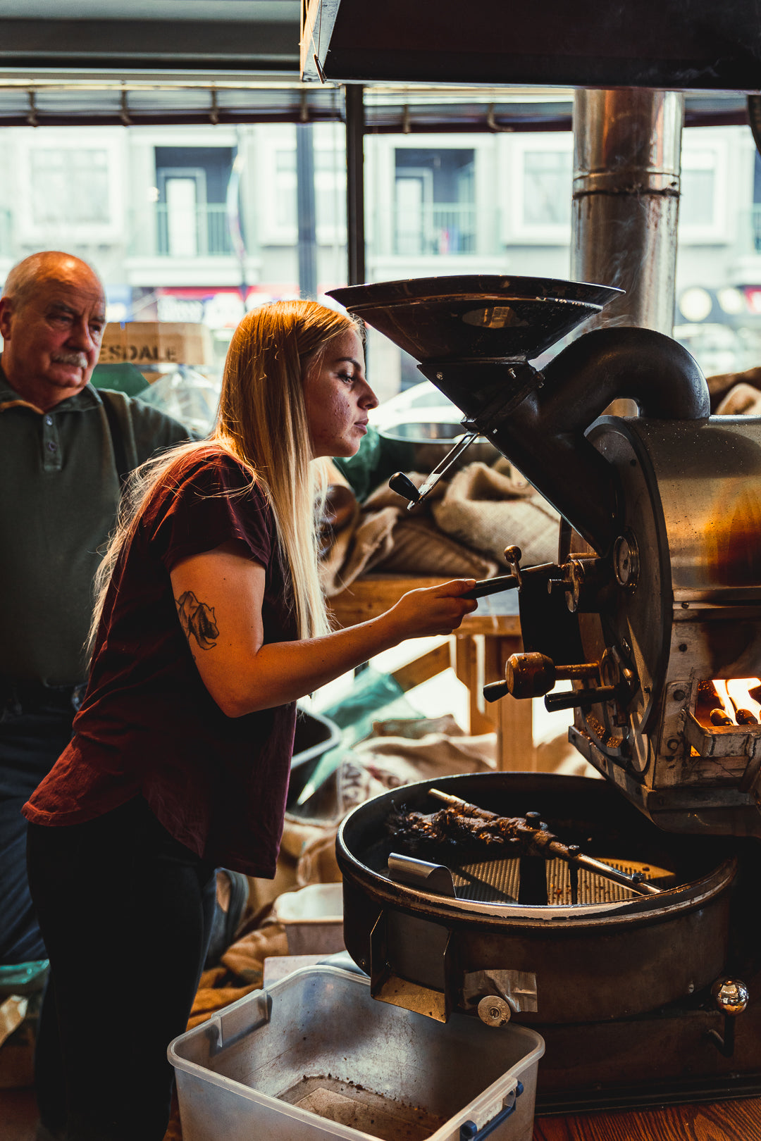 A roaster watching his student while roasting batch of espresso by an antique coffee roaster.