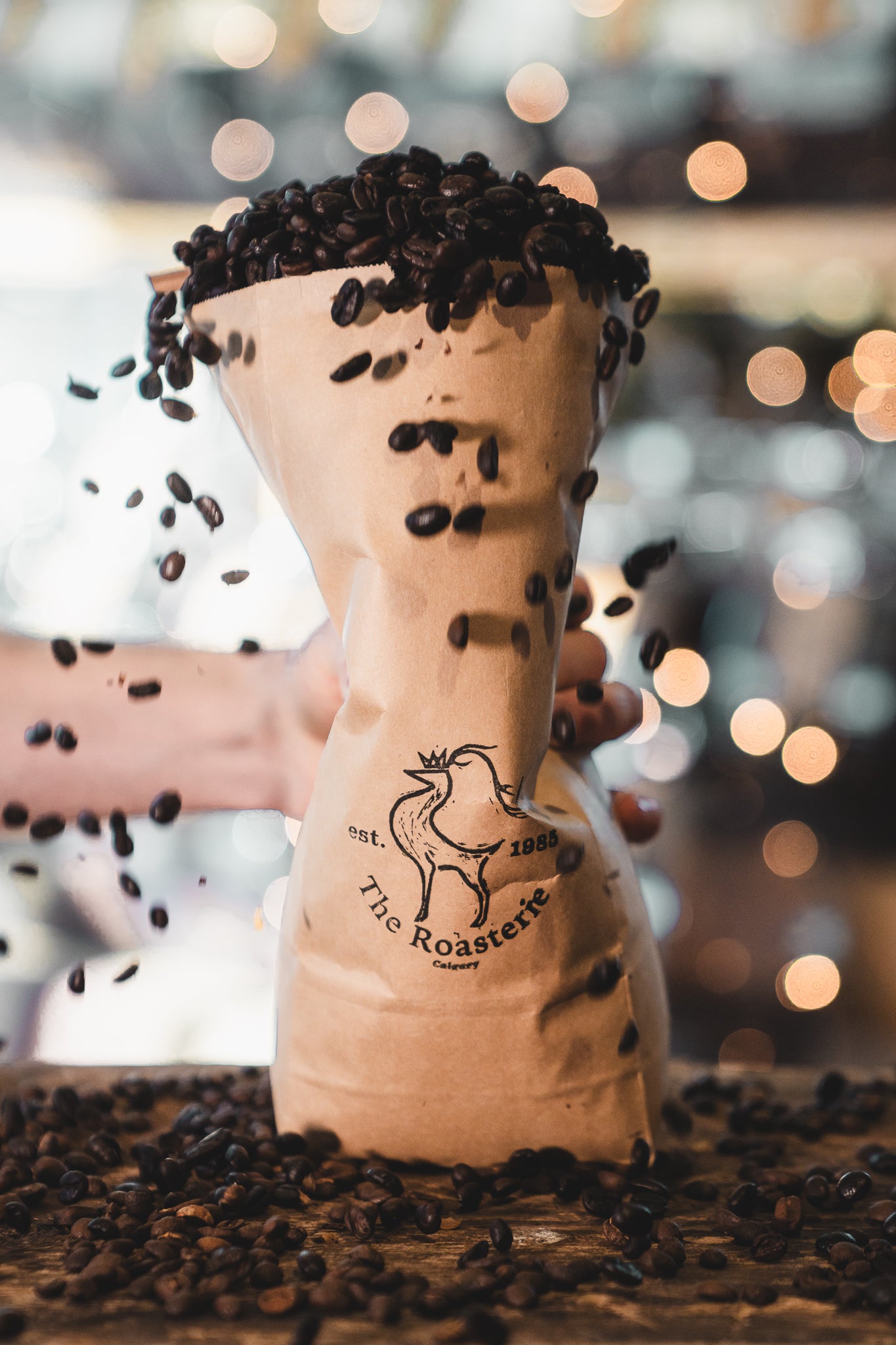 A coffee bag being squished with hand, coffee beans are overflowing, falling down from the table and creating a big explosion.
